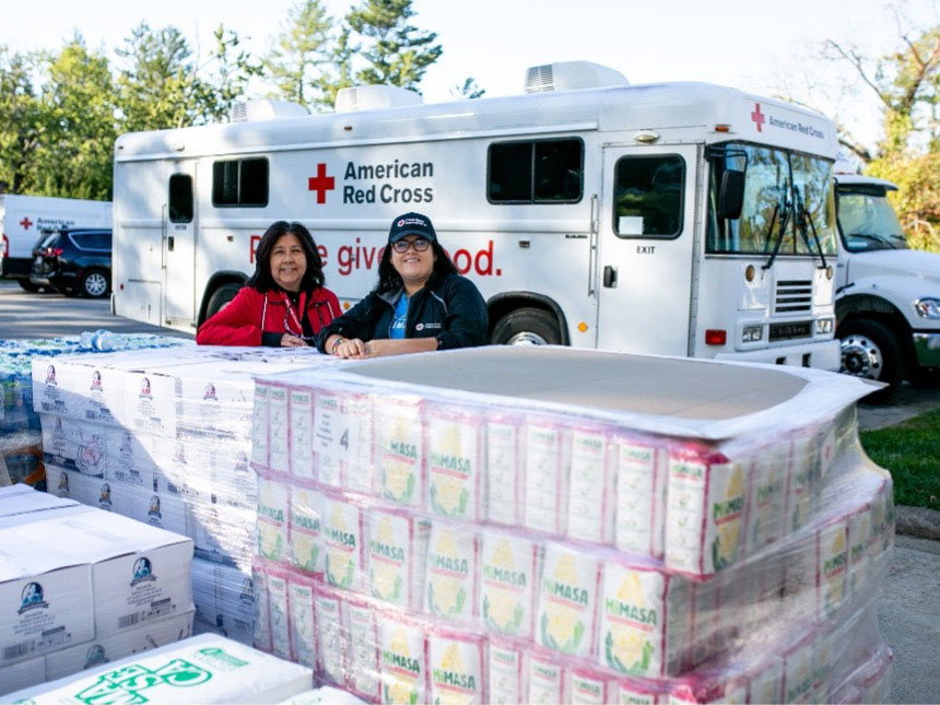 Photo of Mariana Vimbela and Erica Frausto Aguado standing in front of disaster relief supplies.