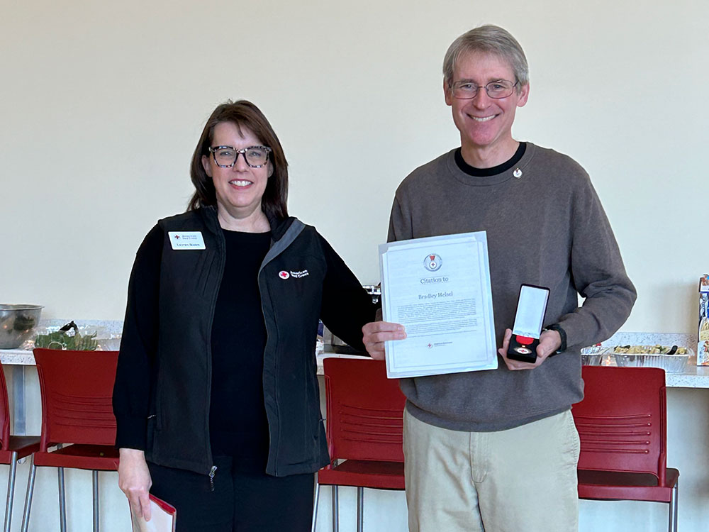 Lejeune High School Teacher displaying his American Red Cross Lifesaving Award while standing next to a Red Cross employee.