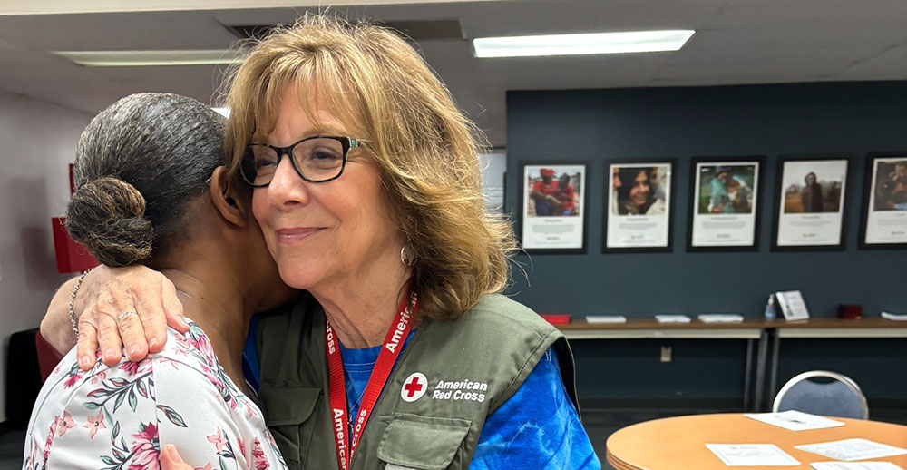 Red Cross worker comforts another person inside an office.