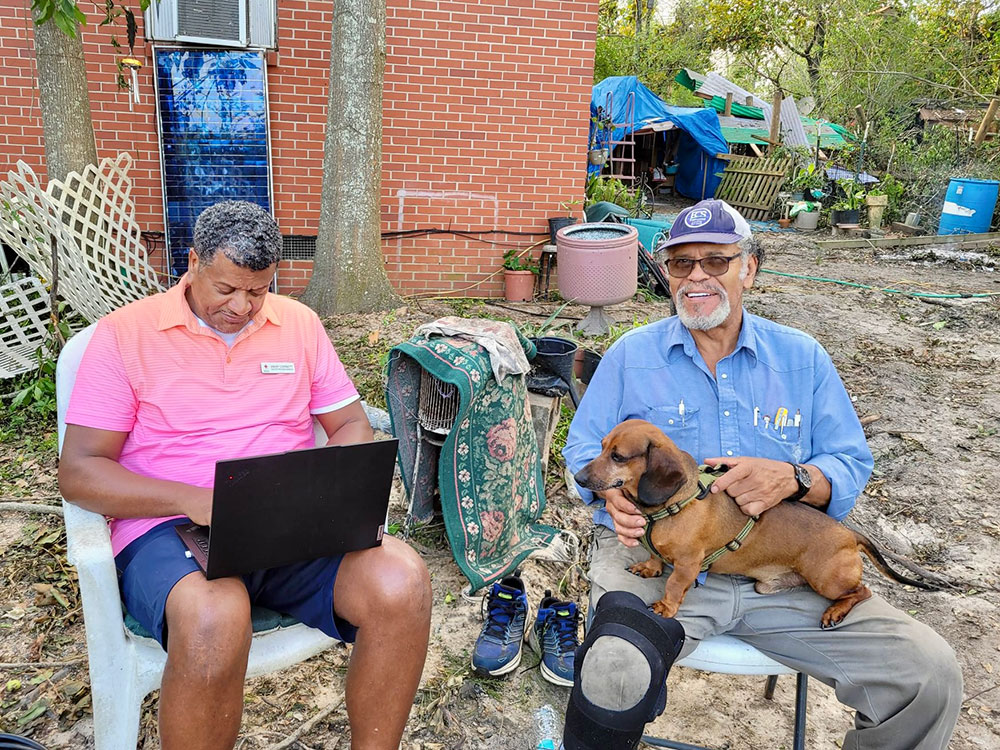 two people sitting in lawn chairs with one working on a laptop and another holding a small dog.