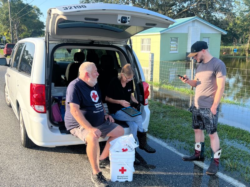 red cross volunteers sitting on back of vehicle.