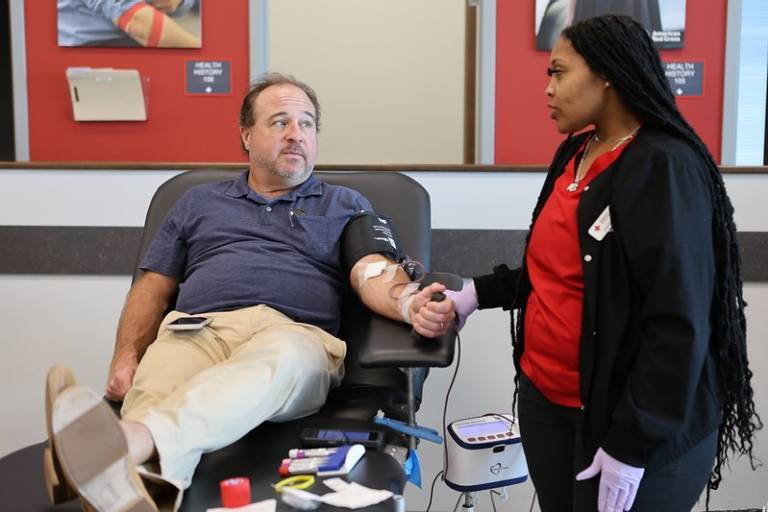 A person sitting on a chair donating blood with a person holding his hand