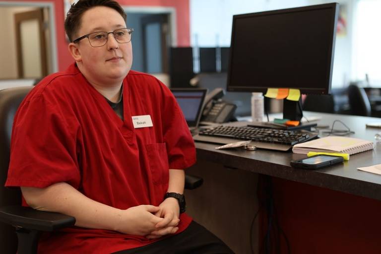 A person in a red scrubs sitting at a desk in front of a computer