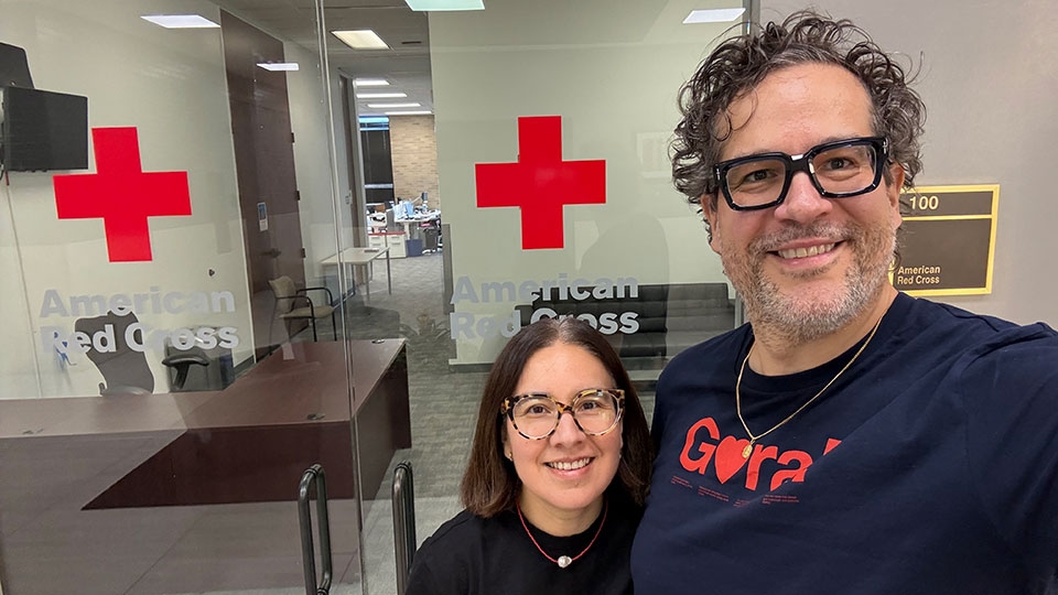 Carla and JP Signoret wearing glasses pose in front of a red cross office.