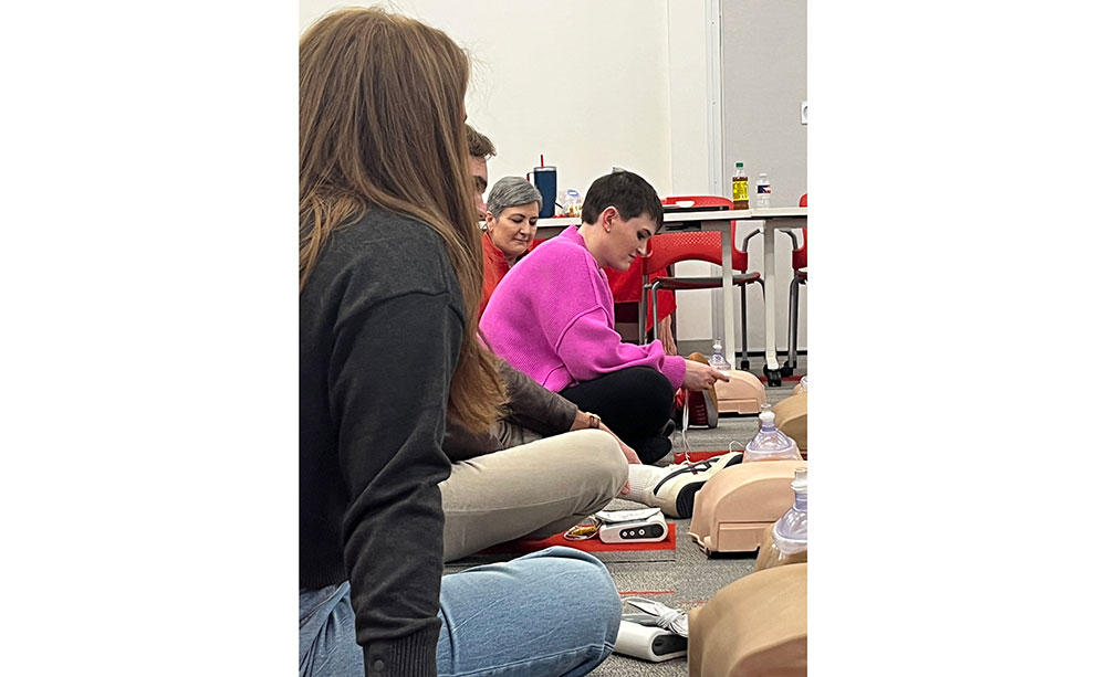 Dallas Caulkins next to a couple other people and a Red Cross staff member training on CPR manikins.