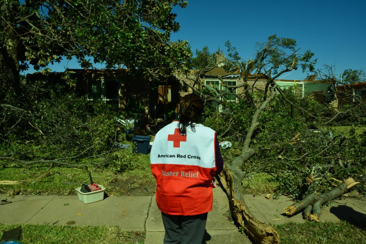 Volunteer stands in front of damaged house after tornado
