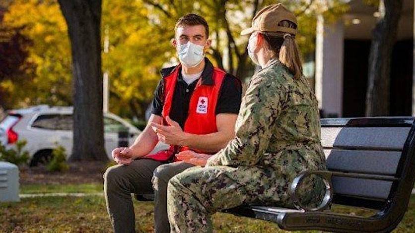 Red Cross volunteer and military personnel sitting on park bench