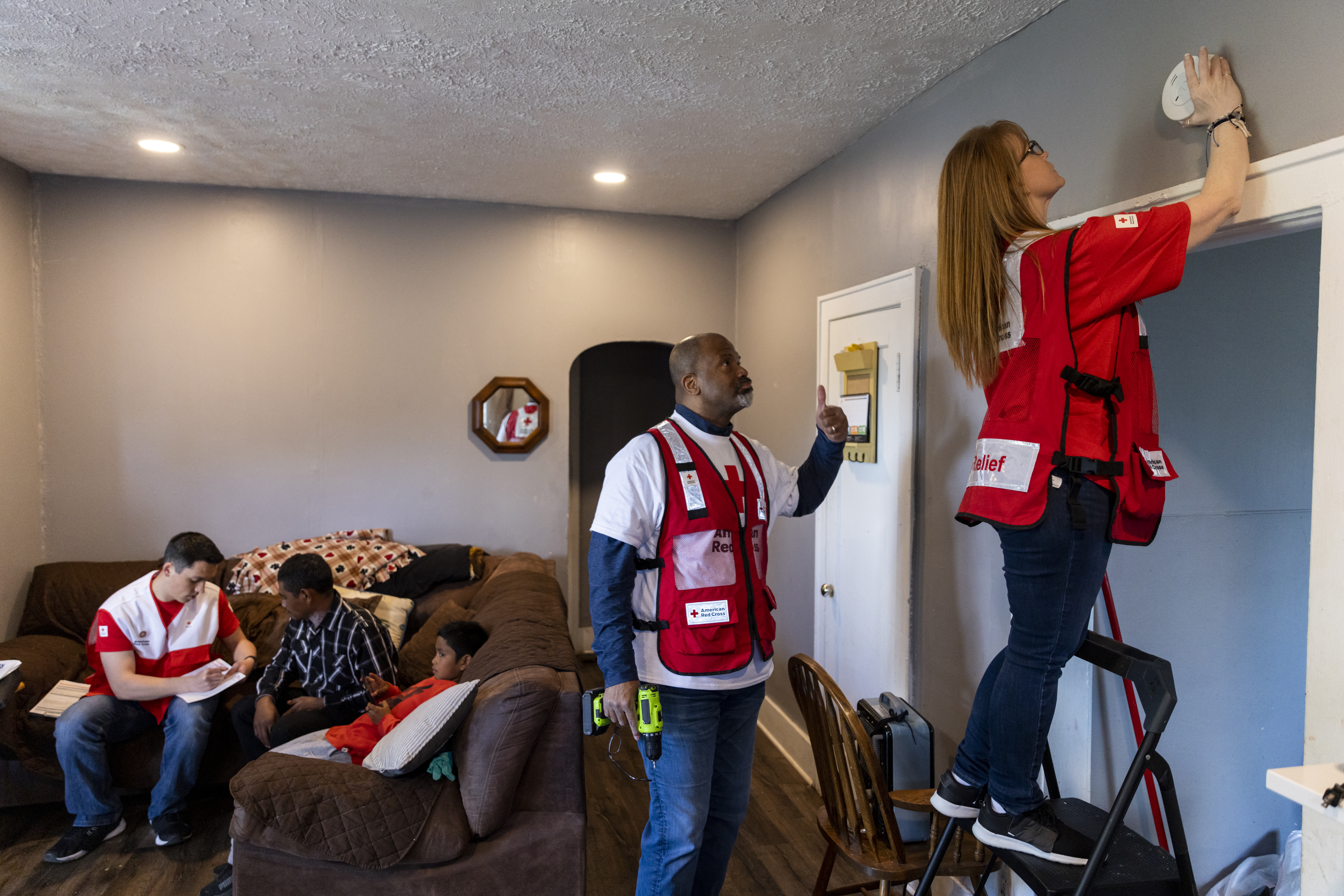 April 29, 2023. Omaha, Nebraska.  American Red Cross volunteers Heidi Briggs and James Boles install a free smoke alarm, while volunteer Nic Wollerman helps resident Juan Carlos Martinez create a home fire escape plan during a Sound the Alarm event in Omaha, Nebraska.  There is nothing better than helping people who need your help, and that is the moment you can do the most good and make an unforgettable difference in your community,  James said.  Photo by Scott Dalton/American Red Cross