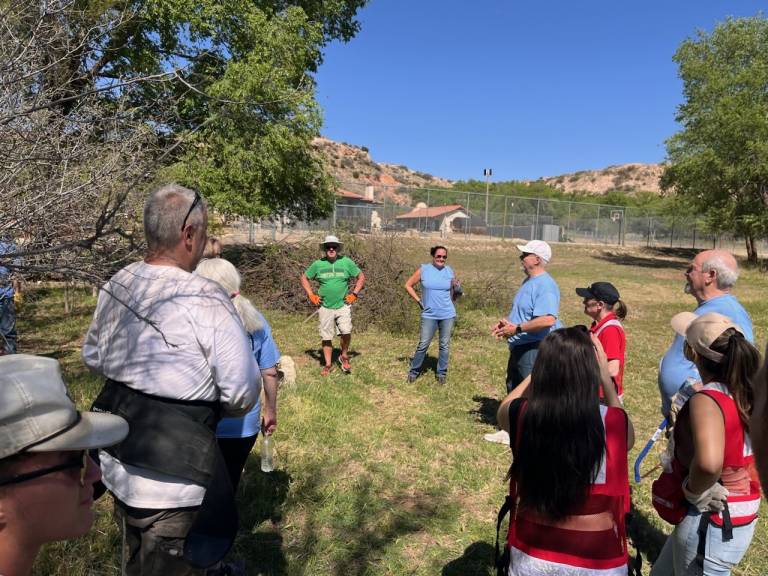group of volunteers in a grassy field listening to someone speaking.