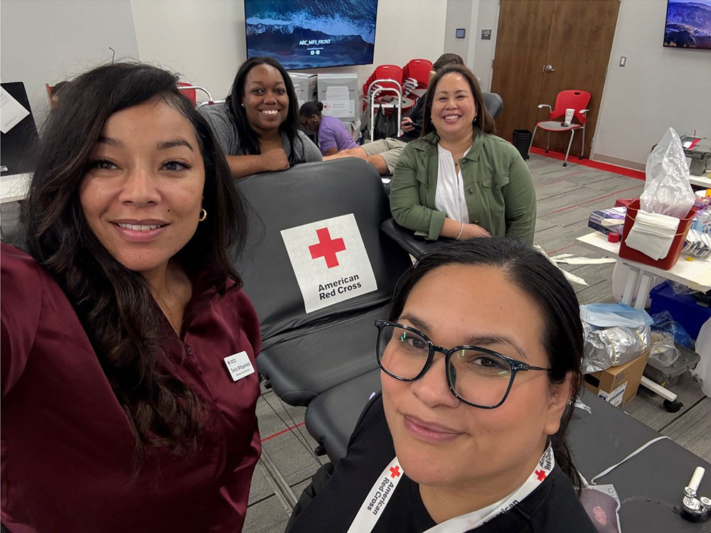 Stephanie, standing next to a Red Cross blood donation chair and three other Red Cross volunteers, at a Red Cross blood drive in August of 2025.