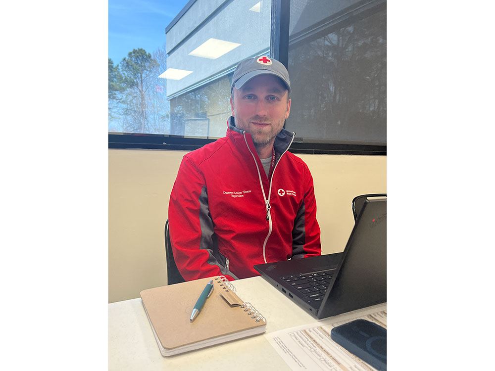 Photo of Andrew Rosenberg wearing a Red Cross hat and jacket while sitting at a desk.