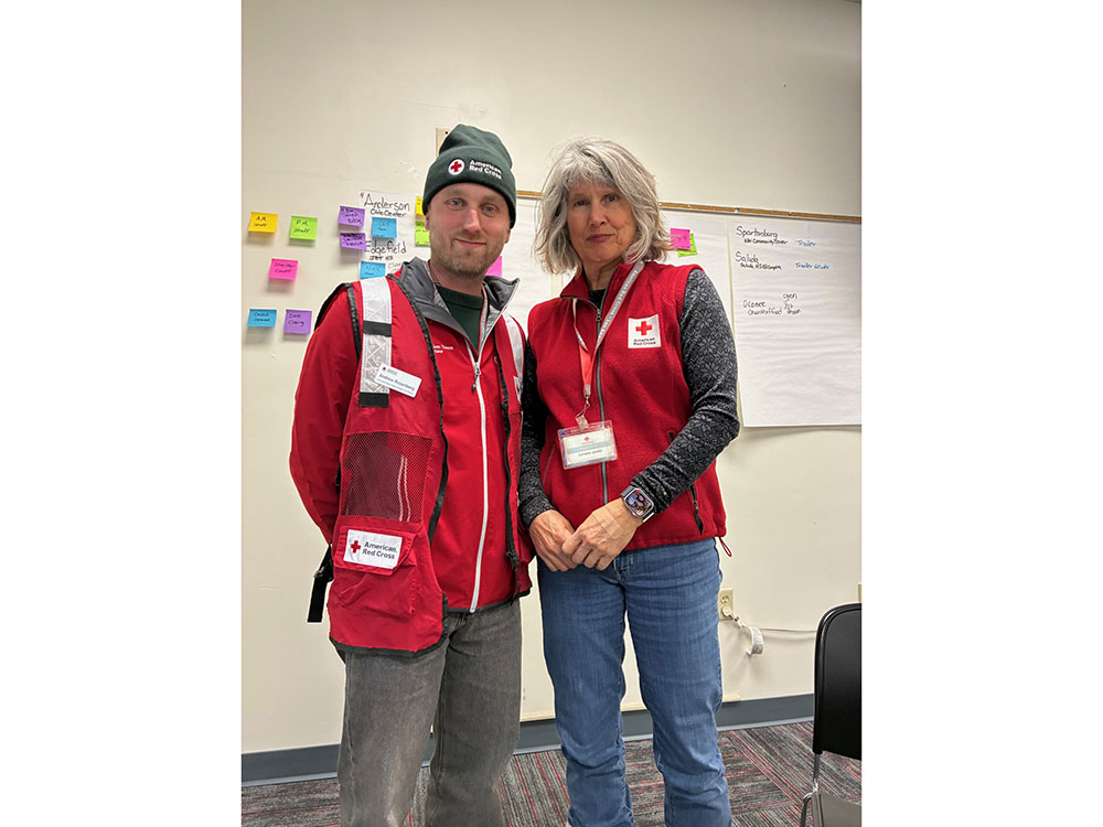 Andrew Rosenberg wearing a Red Cross beanie and jacket, standing next to another Red Cross volunteer.