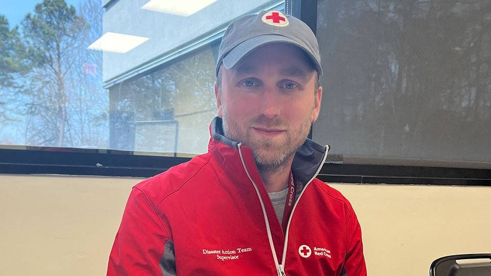 Photo of Andrew Rosenberg wearing a Red Cross hat and jacket while sitting at a desk.