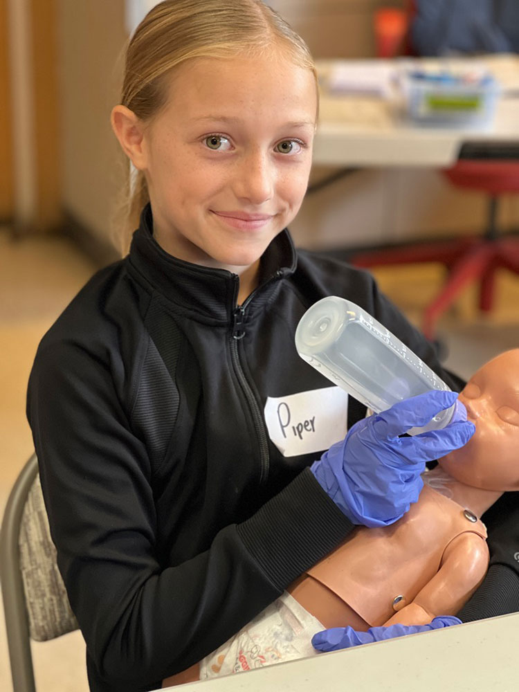 Piper Hanson practices feeding a baby using a mannequin.