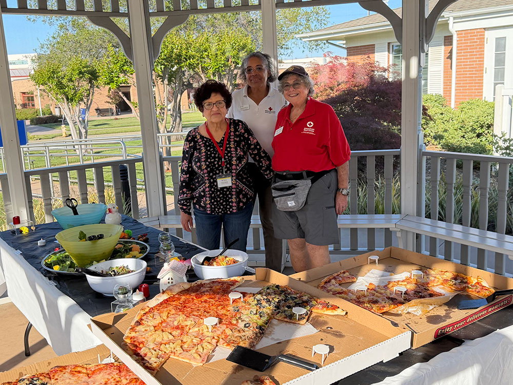 Connie Borrego, Roxanne Anderson and Liz Dietz next to tables with food under a gazebo.