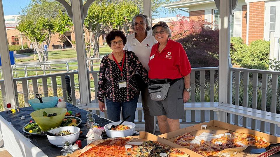 Connie Borrego, Roxanne Anderson and Liz Dietz next to tables with food under a gazebo.