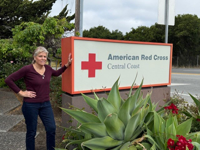 Diane Harris standing next to an American Red Cross Central Coast sign that's by the street.