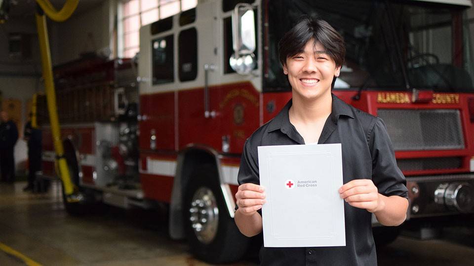Edward Kuan holding the Red Cross Certificate of Extraordinary Personal Action in front of a fire engine.