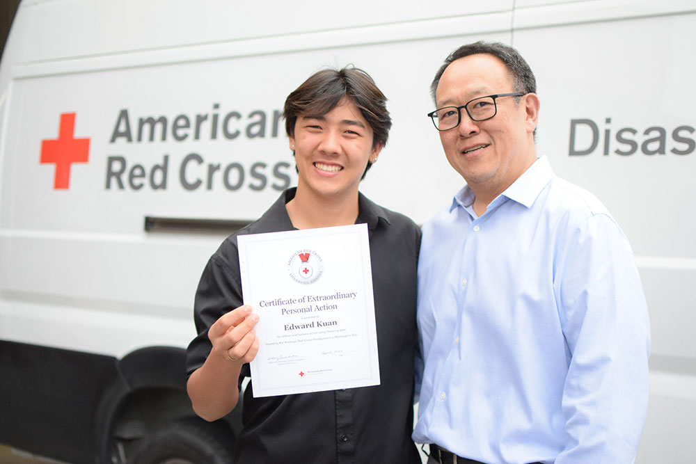 Edward Kuan holding the Red Cross Certificate of Extraordinary Personal Action with his father next to him.