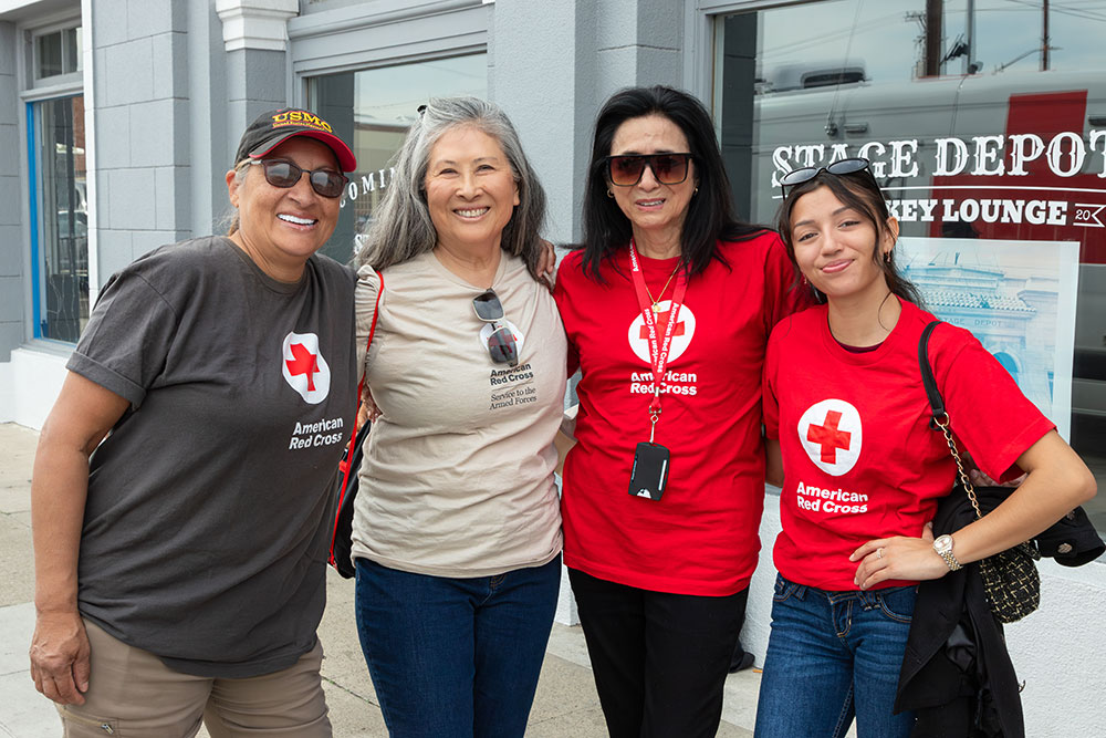 Susan Lugo wearing a hat, sunglasses and a Red Cross shirt stands next to three other Red Cross volunteers.