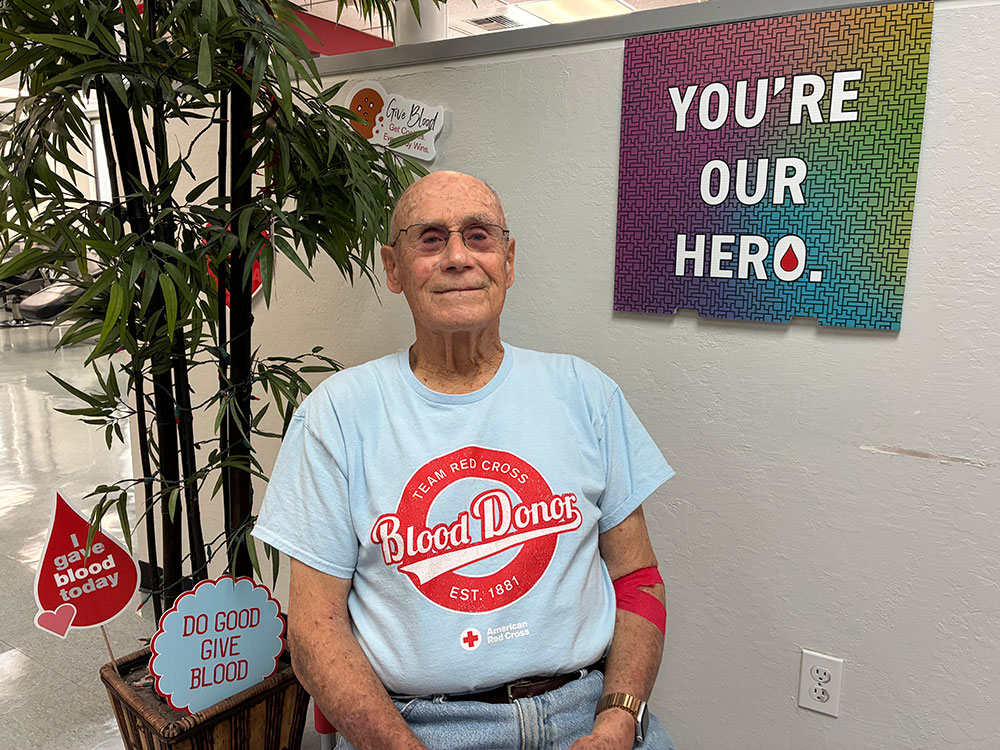 Fred Sullivan after his early morning whole blood donation, next to a planter with donate blood signs.