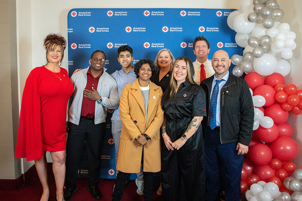 Gerald Golstein and seven other people stand smiling in front of a Red Cross backdrop at a Red Cross event..