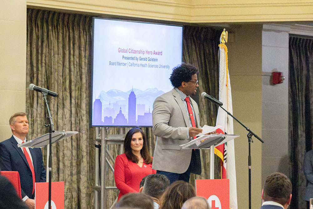 Gerald Golstein speaking on a microphone to a group of people at a Red Cross event.