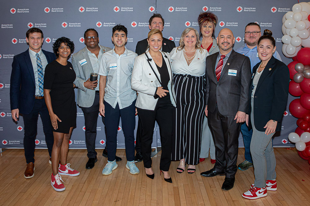 Gerald Golstein and ten other people stand smiling in front of a Red Cross backdrop at a Red Cross event..