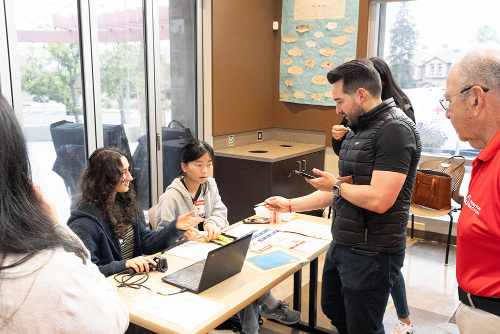 Hadar and Jocelyn sitting at a desk with paperwork and a laptop, with Councilmember Candelas standing in front of the table.