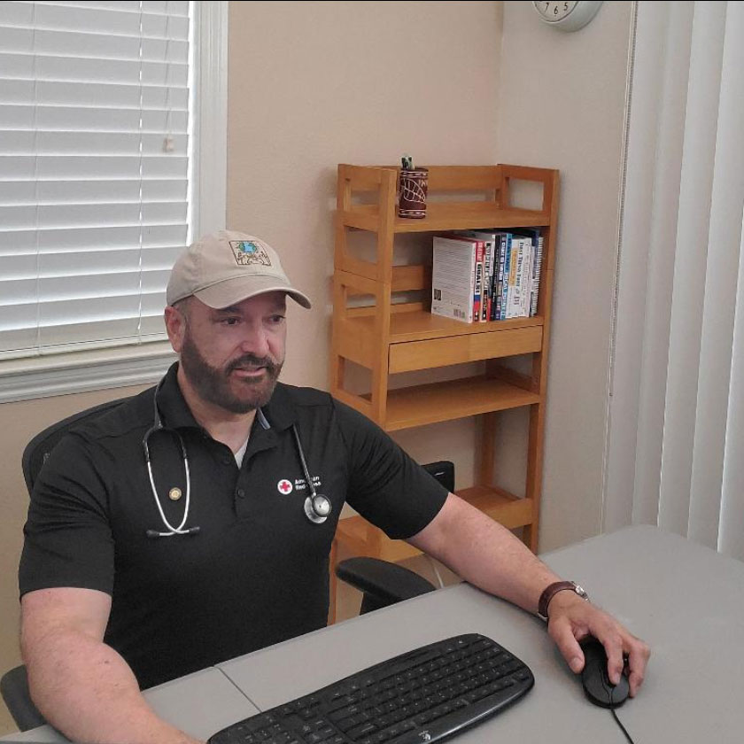 Dr. Bermudez, with a stethoscope around his shoulders, sitting at a desk and working on a computer. 