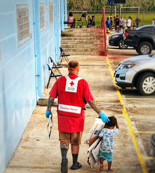 American Red Cross volunteer Jesse Kilgore walking with a child holding folded boxes for mail.