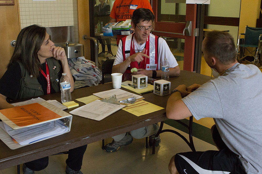 Red Cross volunteers sitting at a table while talking to a man on the other side of the table.