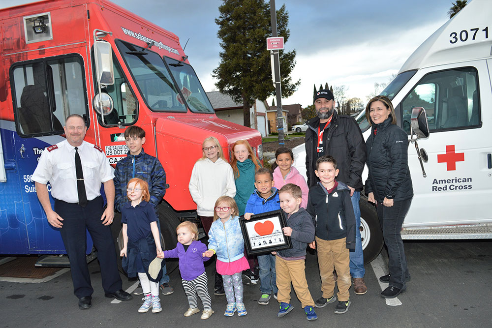 Red Cross volunteers and children group picture in front of a Red Cross van.