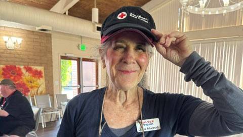 Julie Atwood wearing a Red Cross hat and Halter Project shirt poses in a room, surrounded by soft lighting and neutral-colored walls.
