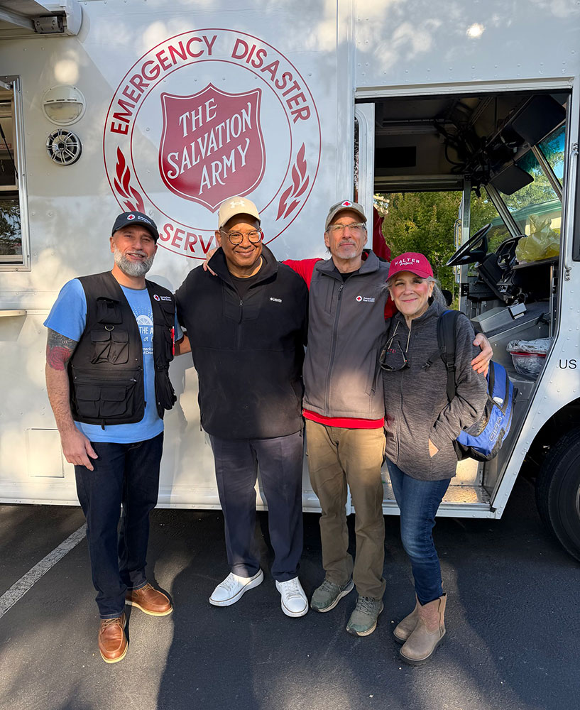 A group of four people poses in front of a Salvation Army truck.