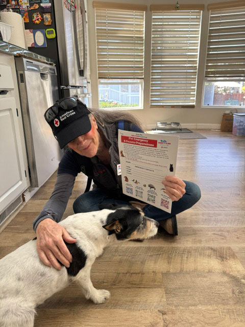 Julie Atwood kneels on the kitchen floor beside a dog while holding a sound the alarm pamphlet.