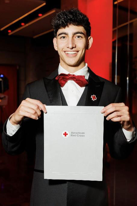 Malik Osman in a suit and bow tie holding his American Red Cross Lifesaving Award for Professional Responders.