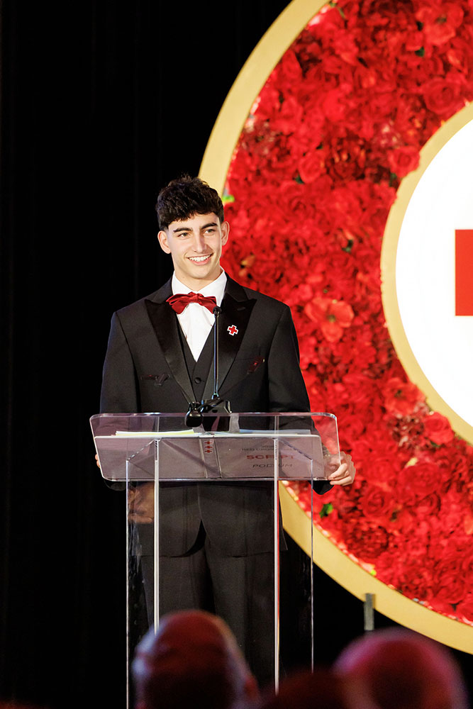 Malik Osman, in suit and bow tie, at a podium accepting his Lifesaving Award at the 2026 Red Cross Gala.