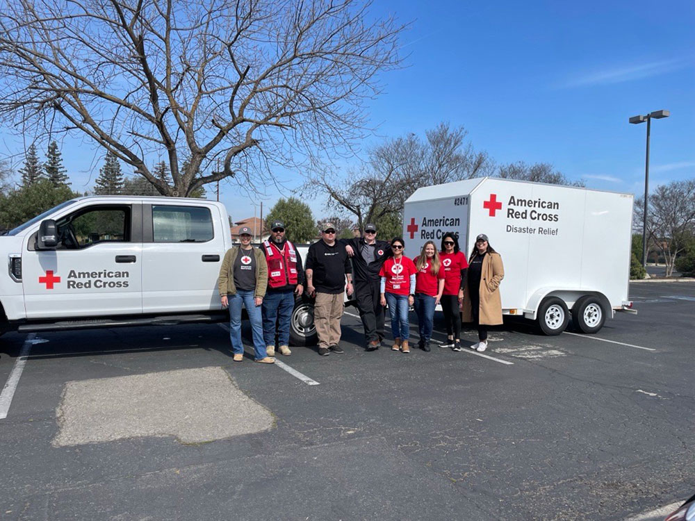 A group picture of eight Red Cross volunteers next to a Red Cross truck and trailer in a parking lot.