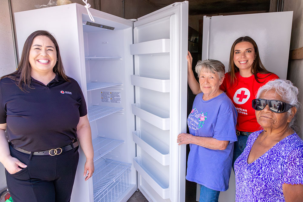 Margarita Moreno and another Red Cross volunteer, stand next to a new freezer and two seniors.