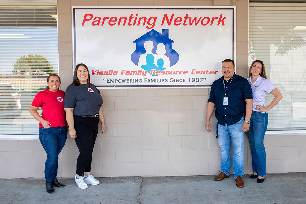 Margarita Moreno and three other Red Cross volunteers stand in front of a Parenting Network sign on the side of a building.