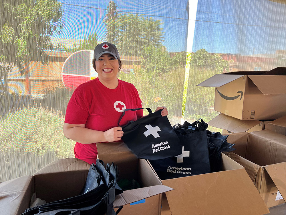 Margarita Moreno, wearing a Red Cross hat and shirt, opens boxes filled with new Red Cross carrying bags.