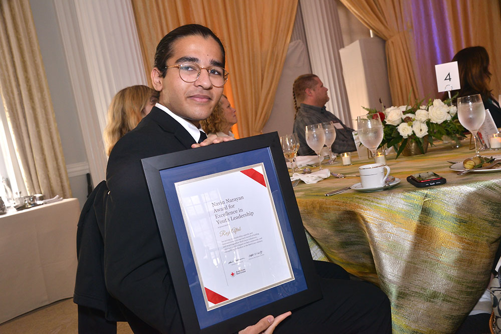 Razi Aftab, in dress clothing at a Red Cross event, holds up a Red Cross award.