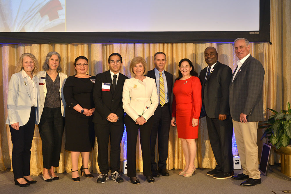 Razi Aftab and eight other people, in dress clothing, standing on a stage, at a Red Cross event.