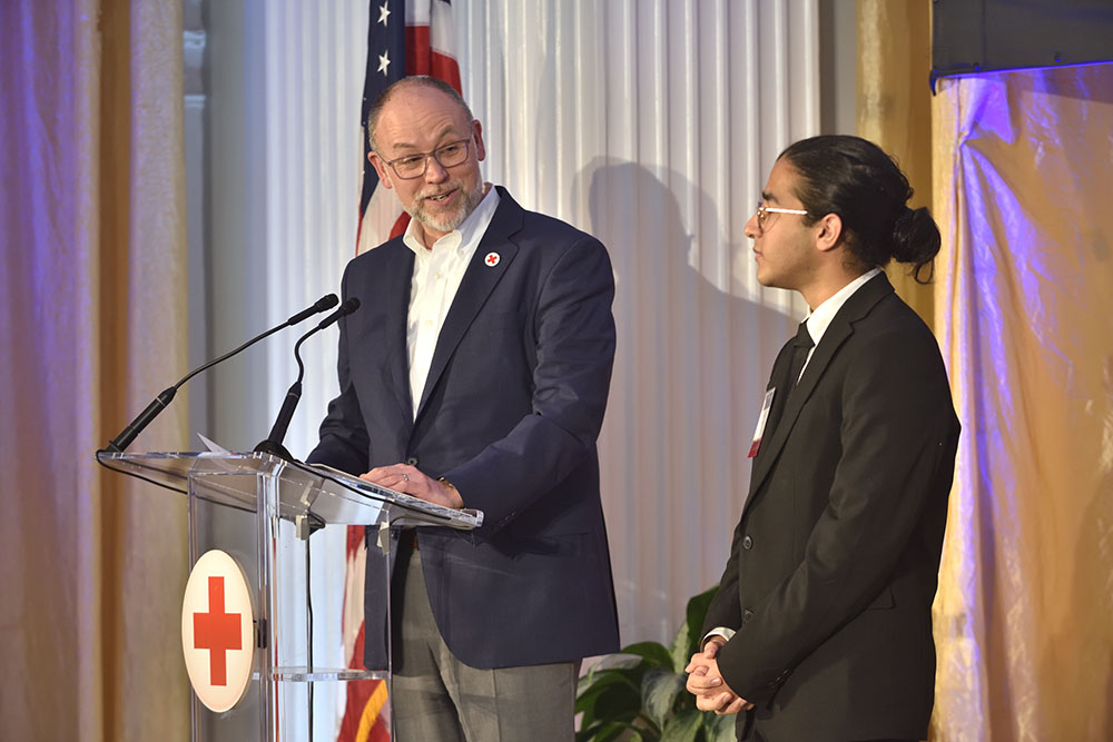 Razi Aftab and a Red Cross employee standing at a podium while looking at Razi, at a Red Cross event.