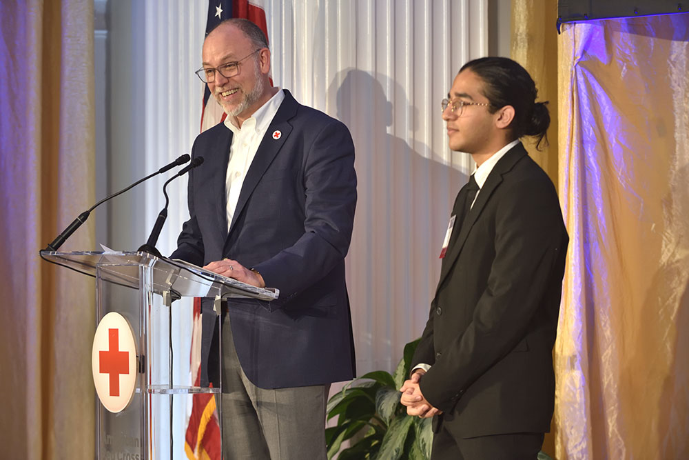 Razi Aftab and a Red Cross employee standing at a podium, at a Red Cross event.