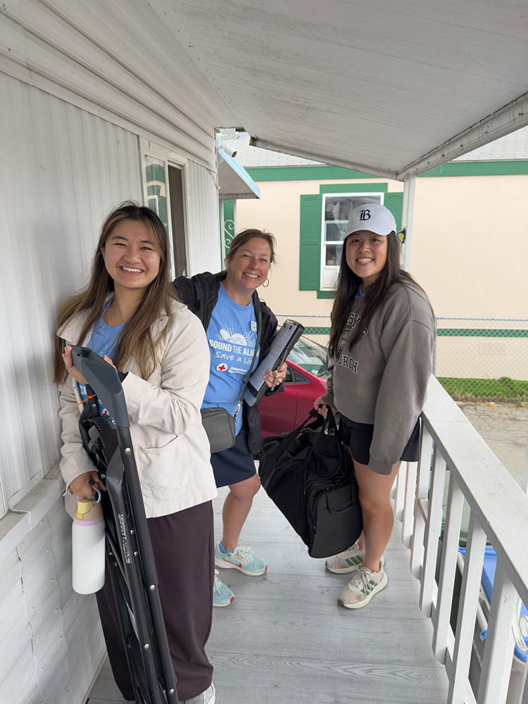 Reagan Lund with her install team smiling stand on a porch, holding equipment and bags