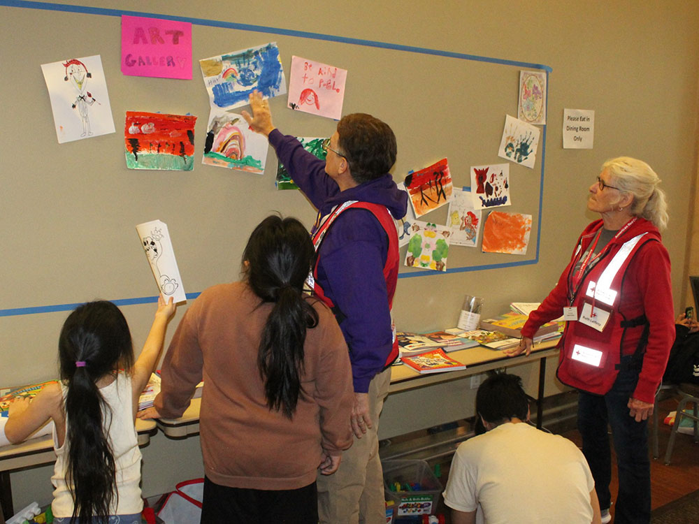 Red Cross volunteers looking at children's paintings on a wall with the children at the shelter.