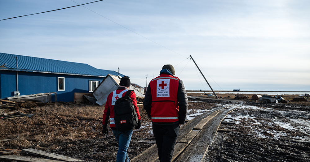 Two Red Crossers walking in the heavily-damaged village of Kipnuk.