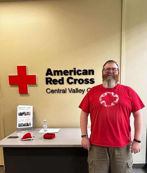Steven Bradley poses for picture while standing next to a Red Cross sign inside a Red Cross office.